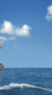 Stones stacked in front of ocean and blue sky.