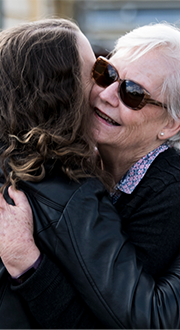 Two people hug outside the ramp access of a town hall building. One is wearing sunglasses.