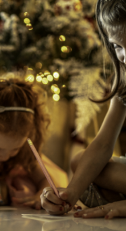 Children writing letters to Santa in front of a Christmas tree.
