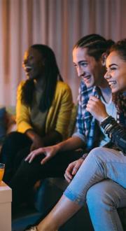 A group of young adults sitting on a couch watching a television which is just out of shot.