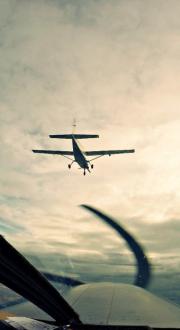 A picture of the underside of a small aeroplane, as seen from another small aeroplane below and behind it.
