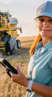Female farmer holding a tablet in a field in front of a combine harvester. 