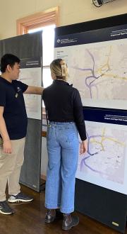A man and woman look at a flight path map on display in a community hall