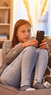 Teen girl sits on couch while browsing on her phone