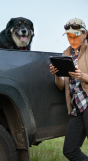 A female farmer leaning against her ute using her laptop