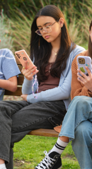 Three young people sitting on park bench, looking at their phones