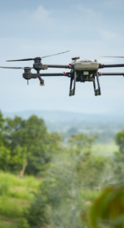 A drone in flight over a green landscape.