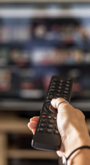 Close up of a person holding a remote control with a television screen in the background.