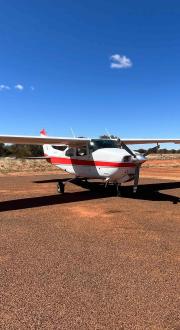 A small plane sitting on a landing strip in a remote area surrounded by red earth.