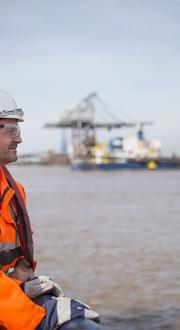 Two maritime workers looking out to sea with a ship in the background.