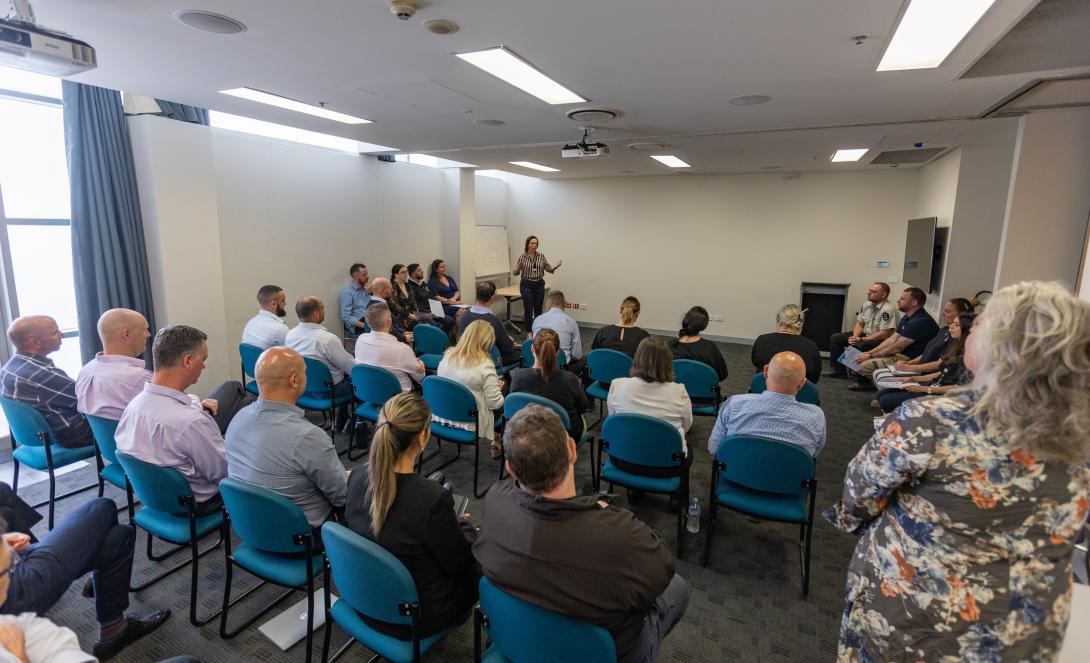 People in a room sitting on blue chairs watching a speaker at the front. Photo credit: Cumberland Council, NSW