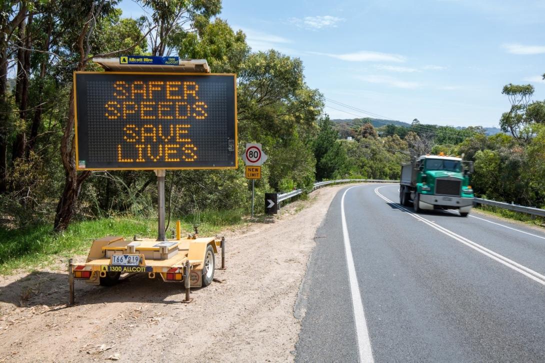 Photo of an 80km/h road with a truck on it with a sign on the side saying “SAFER SPEEDS SAVE LIVES”. Photo credit: Mornington Peninsula Shire Council, VIC