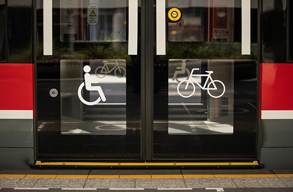 •	Image of tram doors with the international symbol of accessibility on the left door and an image of a bike on the right door.