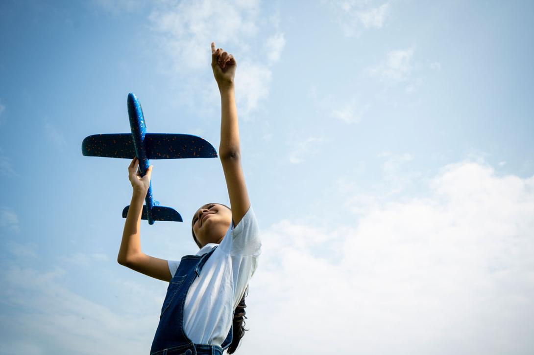 Girl playing with a toy airplane against a blue sky